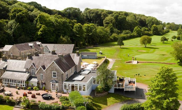 Charming stone manor nestled in lush countryside, with a sunlit terrace, conservatory, and golf course views. Surrounded by trees and rolling greens,